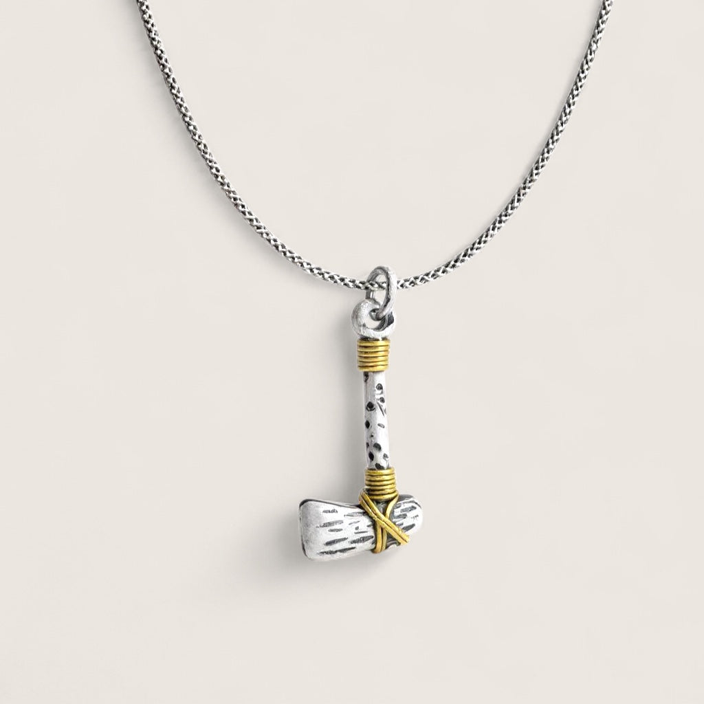 Silver and gold axe-shaped pendant on a chain against a light background