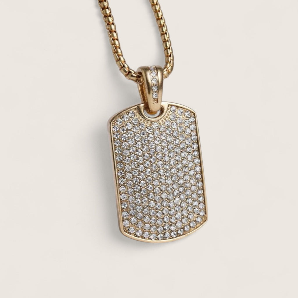 Gold necklace with a diamond-encrusted dog tag on a beige background