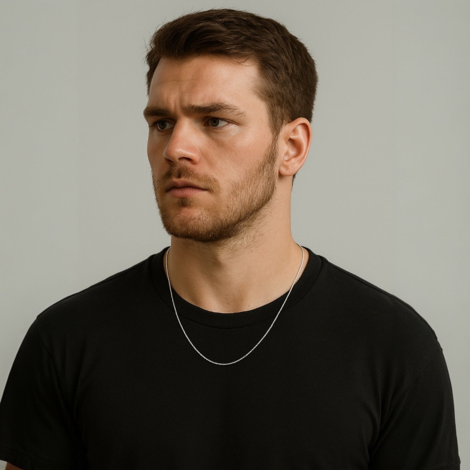 Man wearing a black t-shirt and silver necklace against a plain background