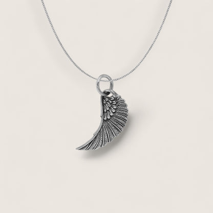 Silver wing-shaped pendant on a chain against a light gray background